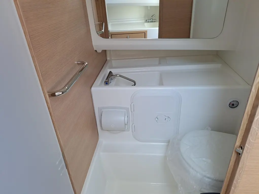 Compact bathroom with a toilet, sink, and mirror; wooden accents and a convenient grab handle visible in the design.